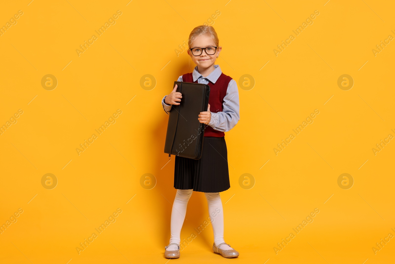 Photo of Little girl with glasses and briefcase on orange background. Dreaming of future profession