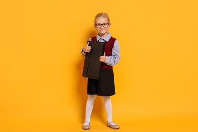 Photo of Little girl with glasses and briefcase on orange background. Dreaming of future profession