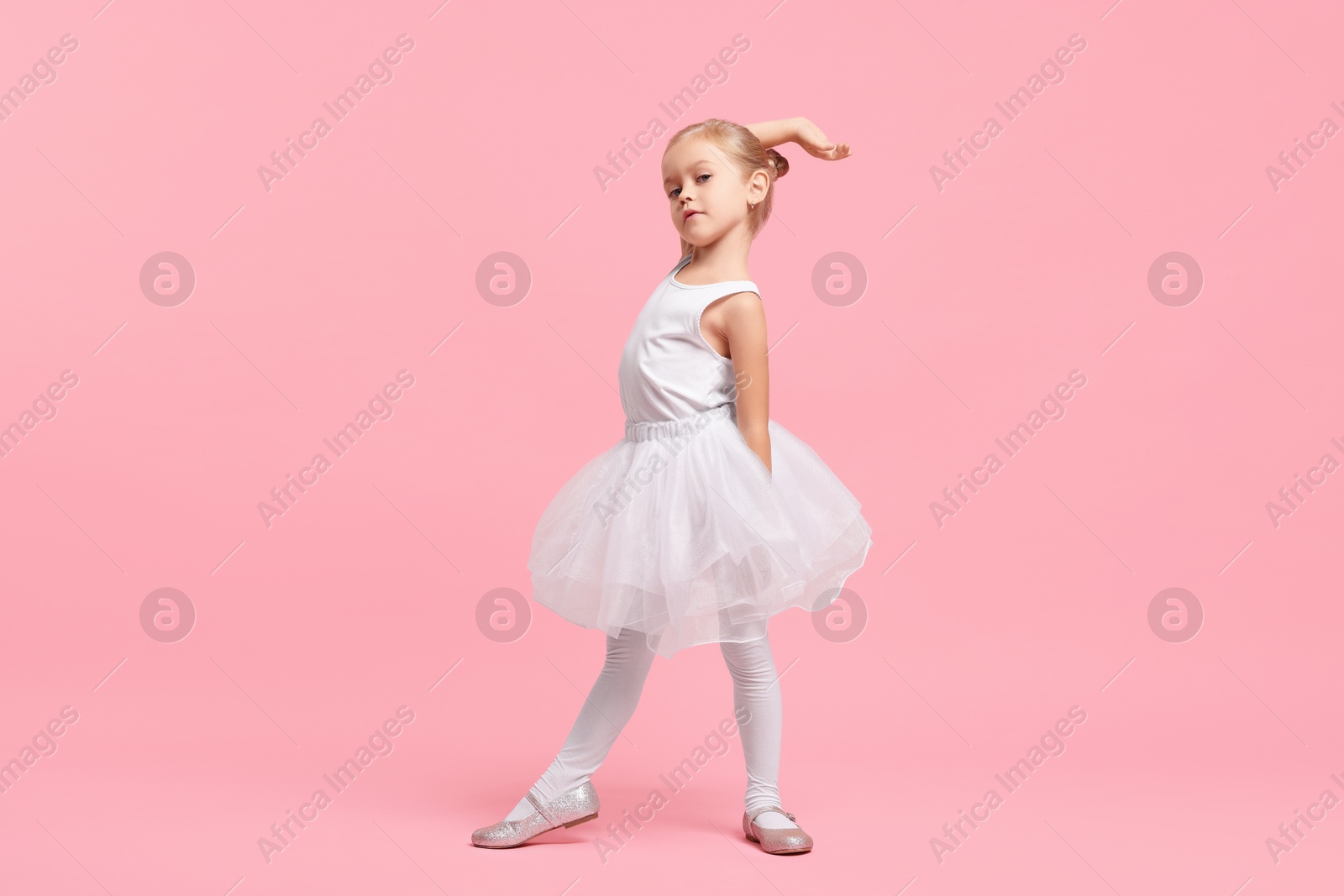 Photo of Little girl pretending to be ballerina on pink background. Dreaming of future profession