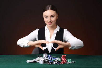 Photo of Professional croupier with chips shuffling playing cards at gambling table on color background