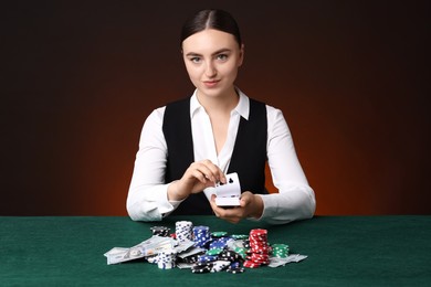 Photo of Professional croupier with chips shuffling playing cards at gambling table on color background