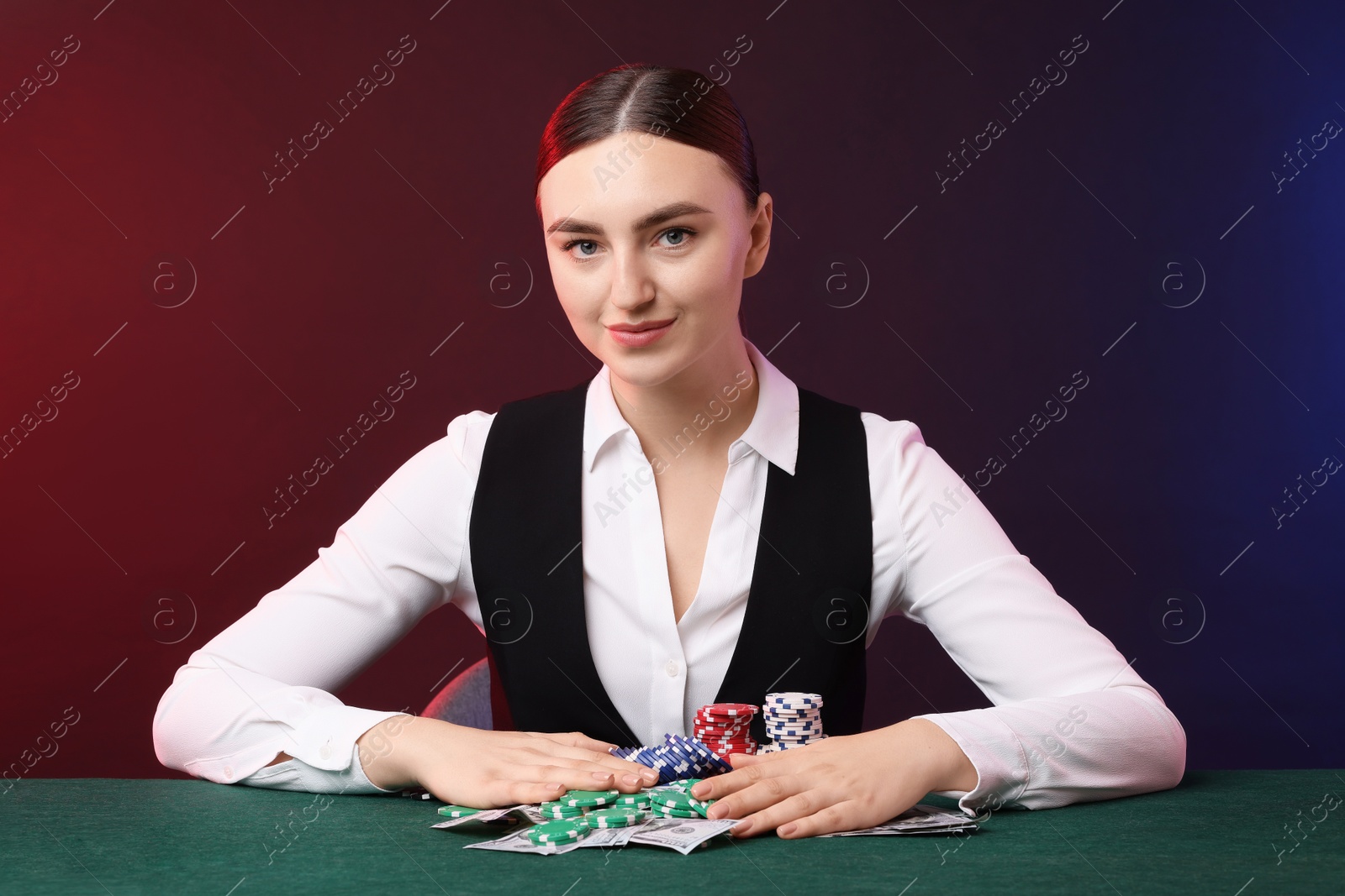 Photo of Professional croupier with casino chips and playing cards at gambling table on color background