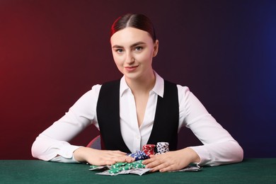 Photo of Professional croupier with casino chips and playing cards at gambling table on color background