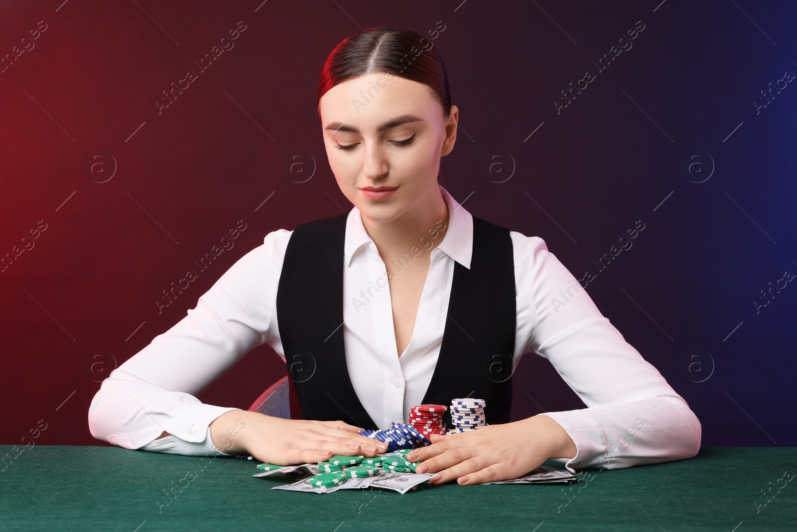 Photo of Professional croupier with casino chips and playing cards at gambling table on color background