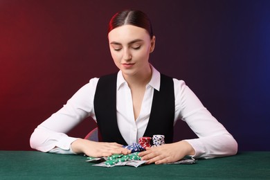 Professional croupier with casino chips and playing cards at gambling table on color background