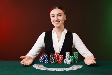 Photo of Professional croupier with casino chips and playing cards at gambling table on color background