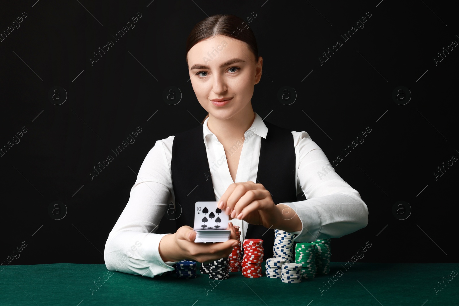 Photo of Professional croupier with chips shuffling playing cards at gambling table on black background