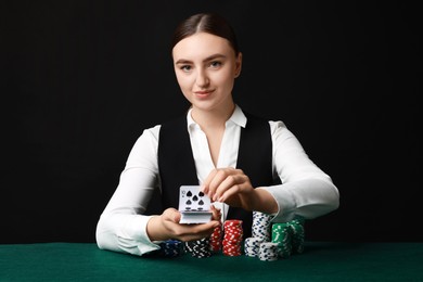 Photo of Professional croupier with chips shuffling playing cards at gambling table on black background