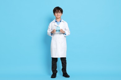 Boy with test tubes pretending to be scientist on light blue background. Dreaming of future profession