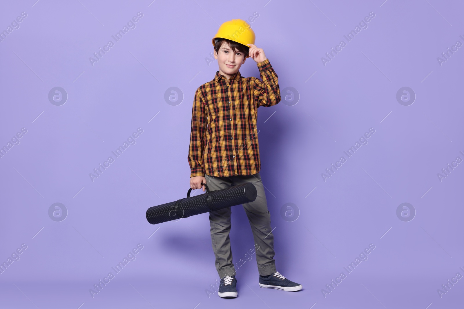 Photo of Boy with blueprint tube pretending to be architect on violet background. Dreaming of future profession