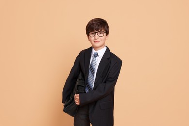 Photo of Boy in suit pretending to be businessman on beige background. Dreaming of future profession