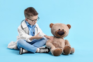 Photo of Little boy with stethoscope and toy pretending to be doctor on light blue background. Dreaming of future profession