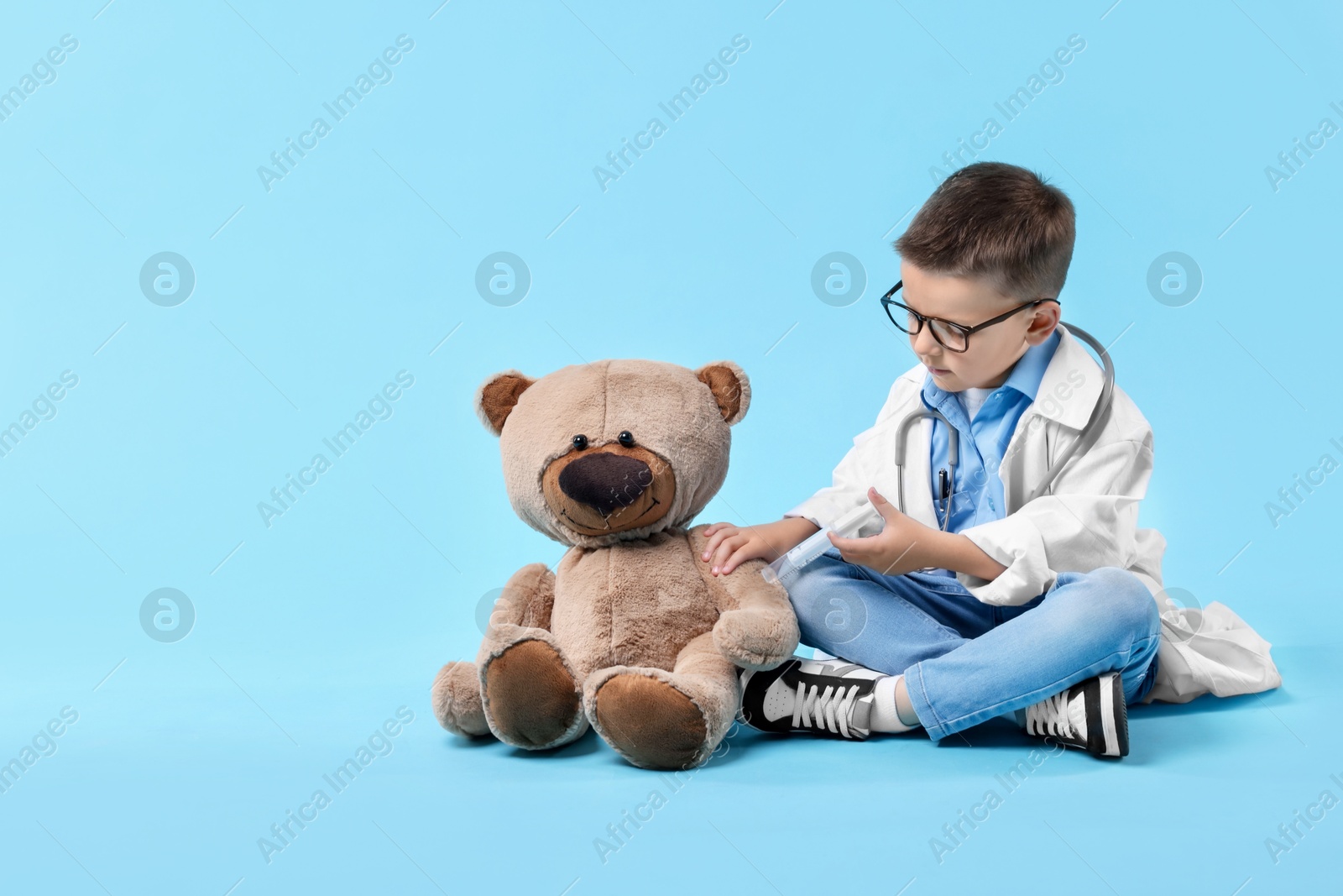 Photo of Little boy with stethoscope and toy pretending to be doctor on light blue background. Dreaming of future profession