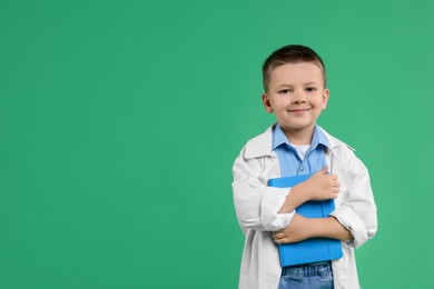 Photo of Little boy with book pretending to be doctor on green background, space for text. Dreaming of future profession