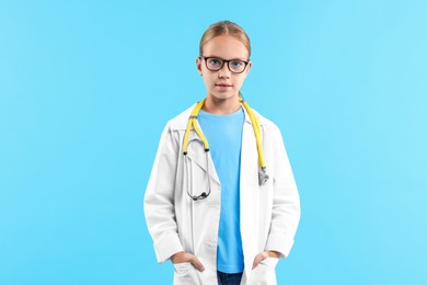 Girl with stethoscope pretending to be doctor on light blue background. Dreaming of future profession