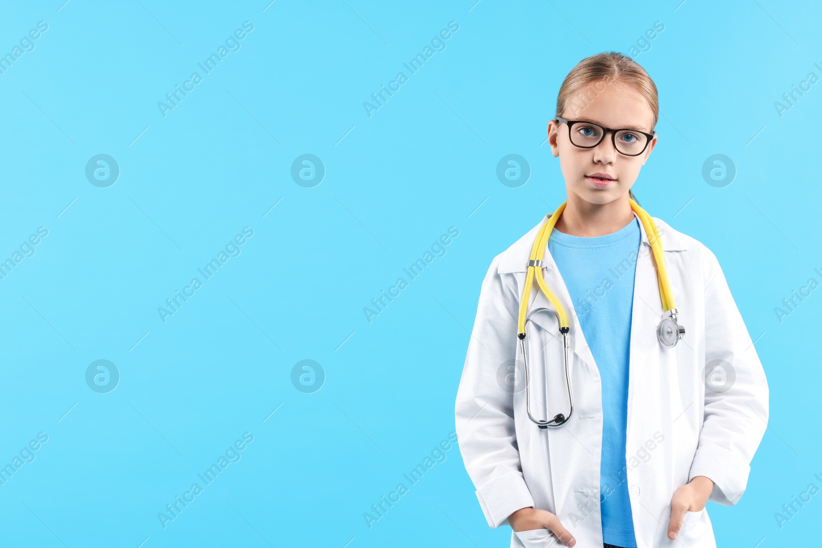 Photo of Girl with stethoscope pretending to be doctor on light blue background, space for text. Dreaming of future profession