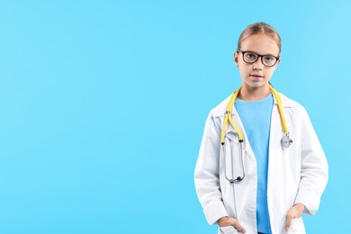 Photo of Girl with stethoscope pretending to be doctor on light blue background, space for text. Dreaming of future profession