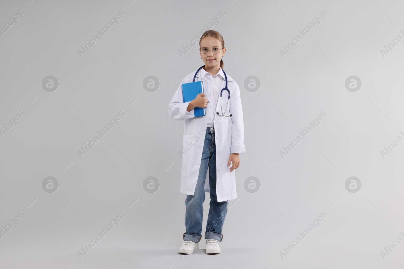 Photo of Girl with stethoscope and book pretending to be doctor on light grey background. Dreaming of future profession