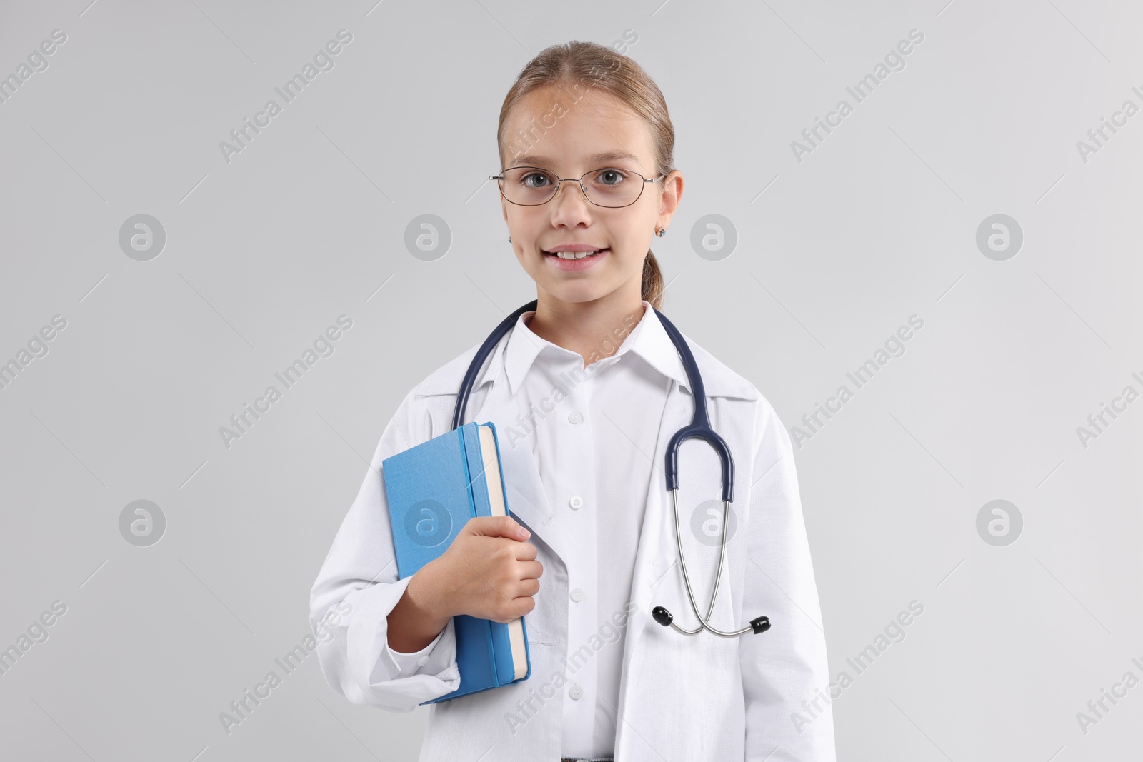 Photo of Girl with stethoscope and book pretending to be doctor on light grey background. Dreaming of future profession