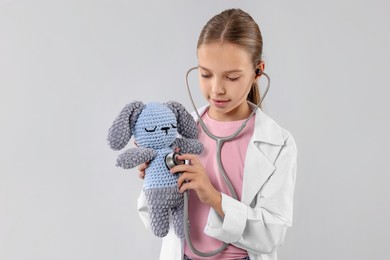 Photo of Girl with stethoscope and toy pretending to be doctor on light grey background. Dreaming of future profession