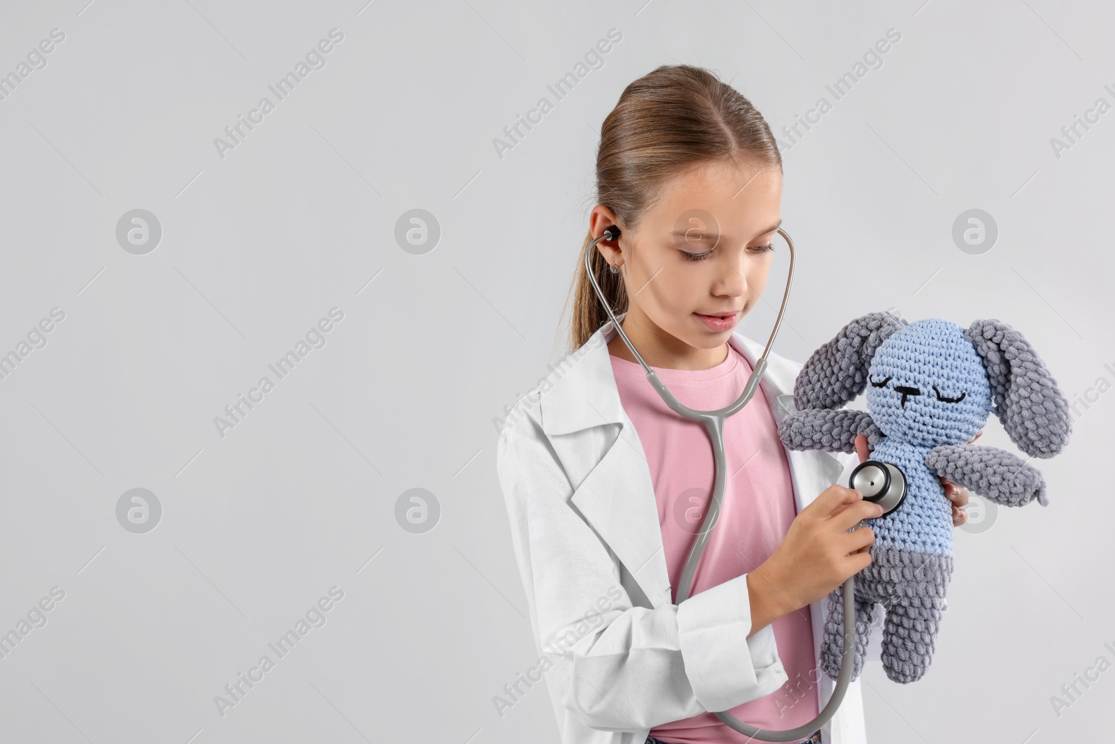 Photo of Girl with stethoscope and toy pretending to be doctor on light grey background, space for text. Dreaming of future profession