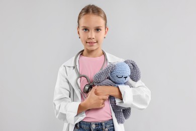 Photo of Girl with stethoscope and toy pretending to be doctor on light grey background. Dreaming of future profession