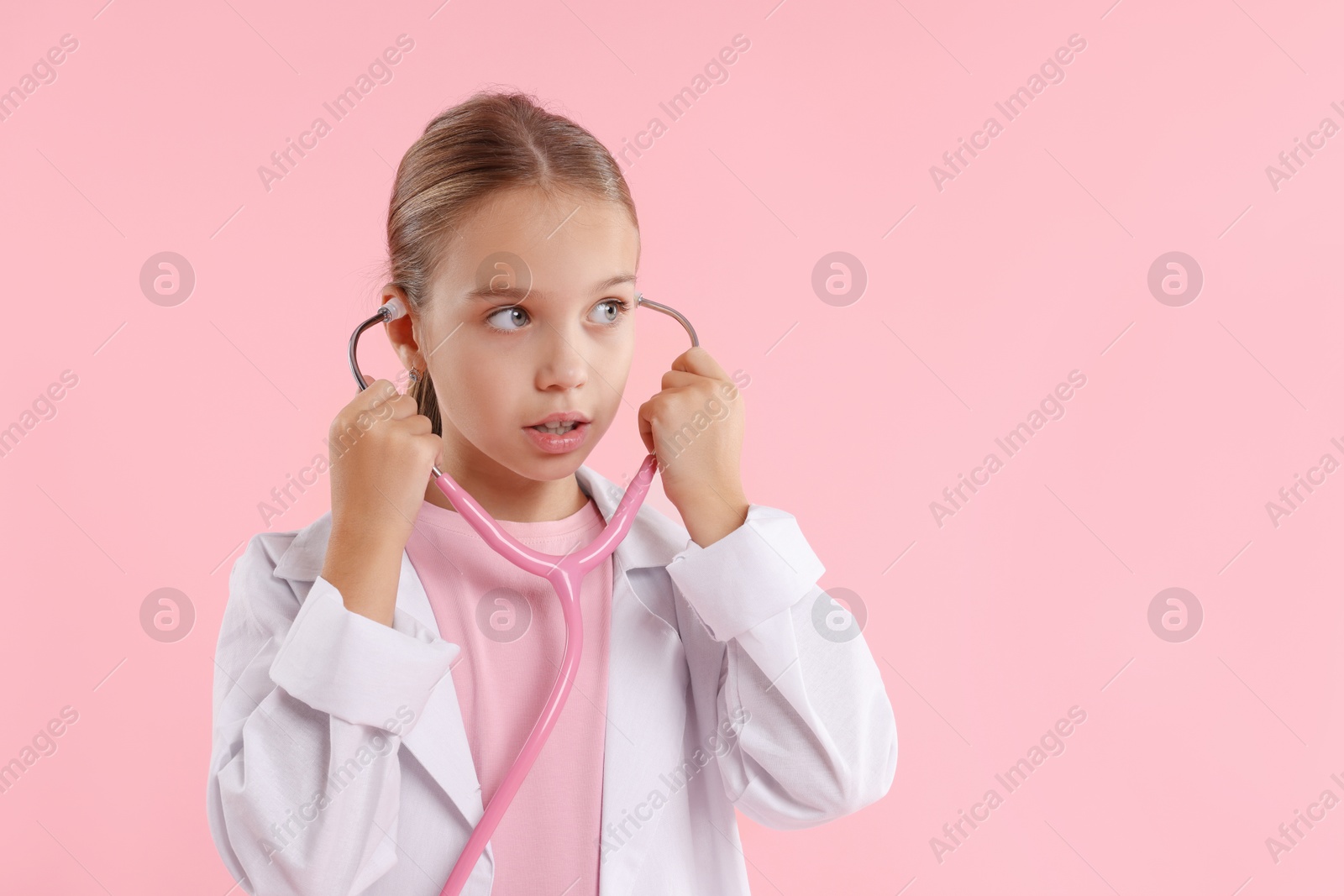 Photo of Girl with stethoscope pretending to be doctor on pink background, space for text. Dreaming of future profession