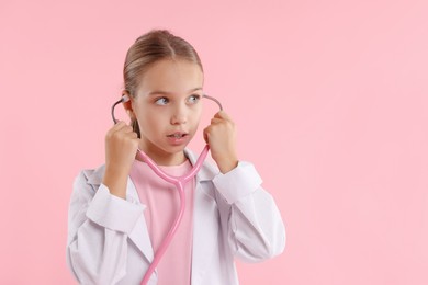 Girl with stethoscope pretending to be doctor on pink background, space for text. Dreaming of future profession