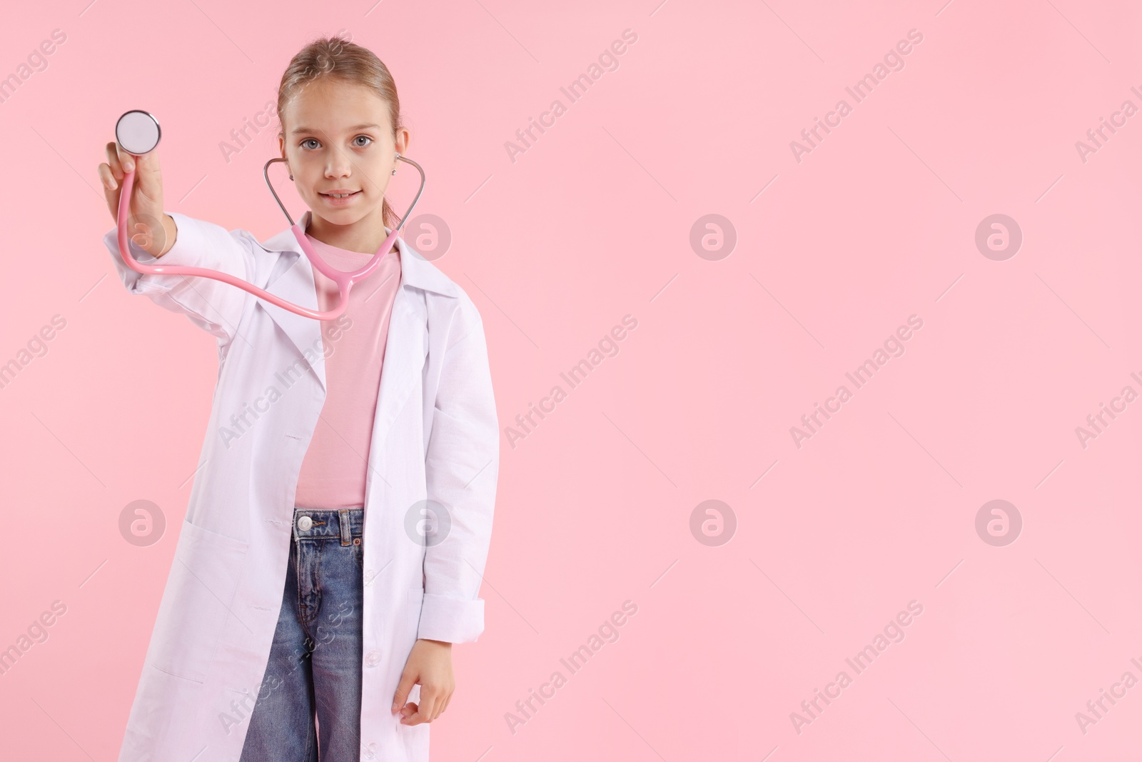 Photo of Girl with stethoscope pretending to be doctor on pink background, space for text. Dreaming of future profession