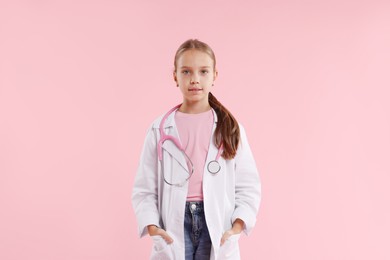 Photo of Girl with stethoscope pretending to be doctor on pink background. Dreaming of future profession