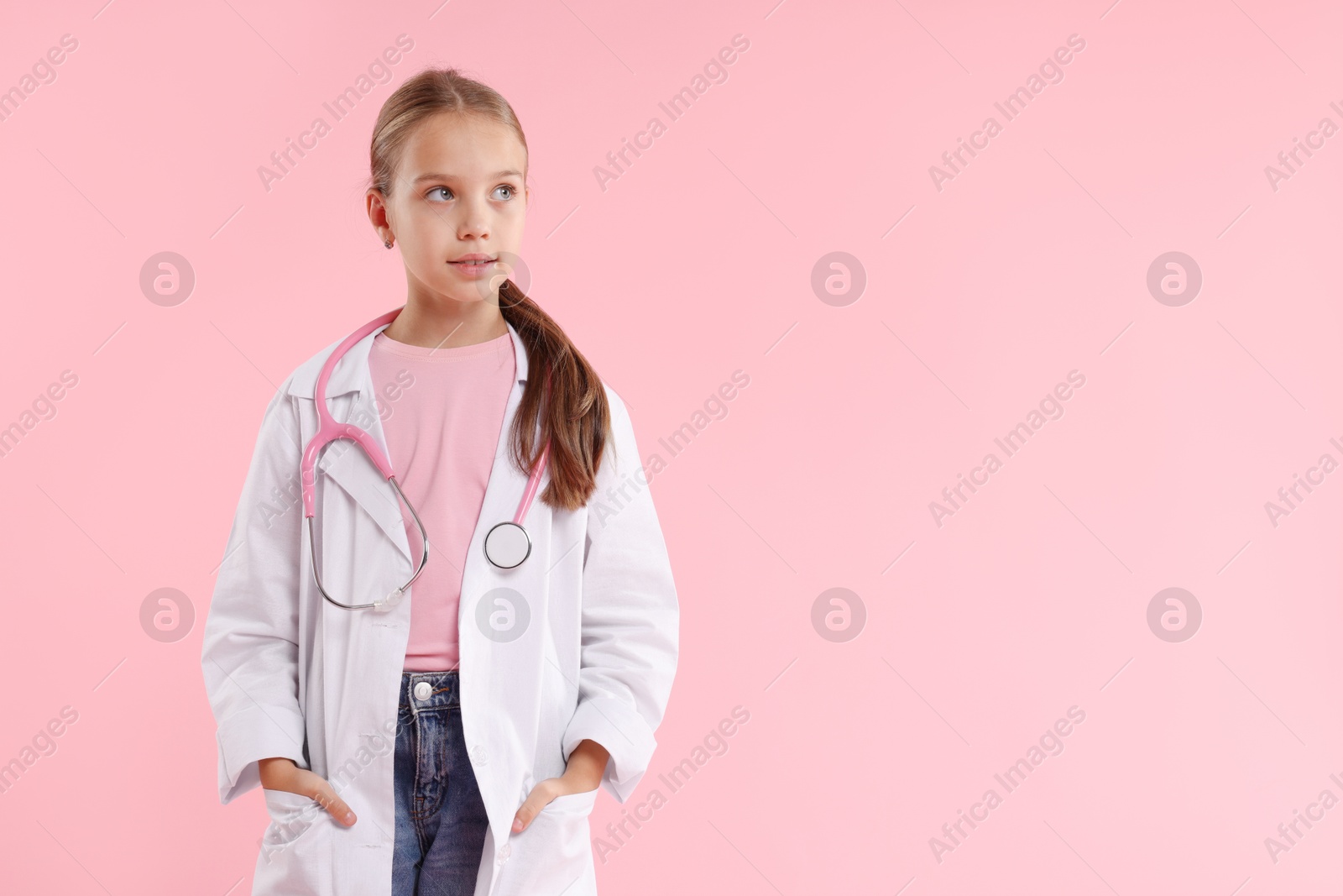 Photo of Girl with stethoscope pretending to be doctor on pink background, space for text. Dreaming of future profession