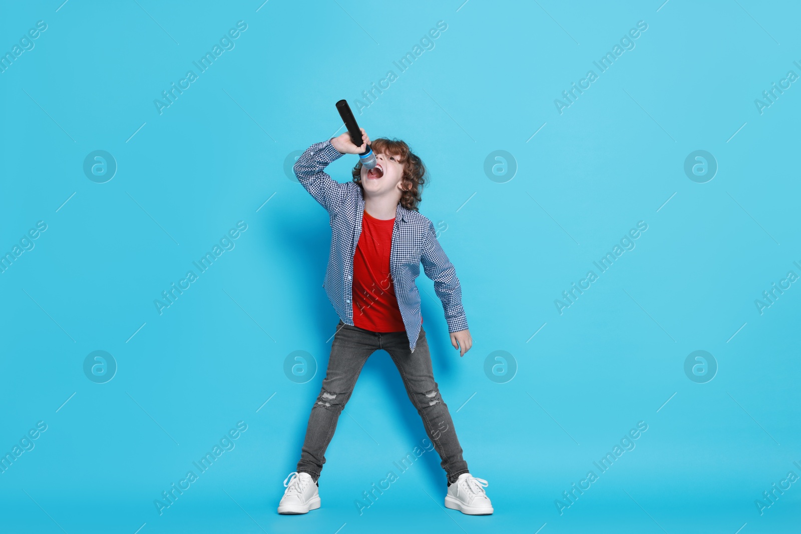 Photo of Little boy with microphone pretending to be singer on light blue background. Dreaming about future profession