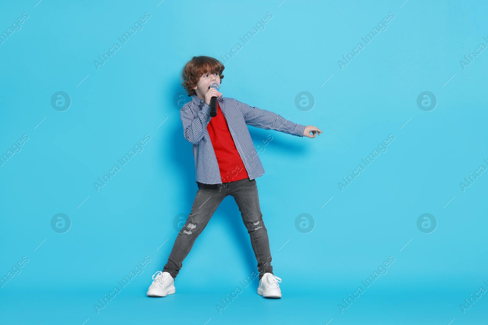 Photo of Little boy with microphone pretending to be singer on light blue background. Dreaming about future profession