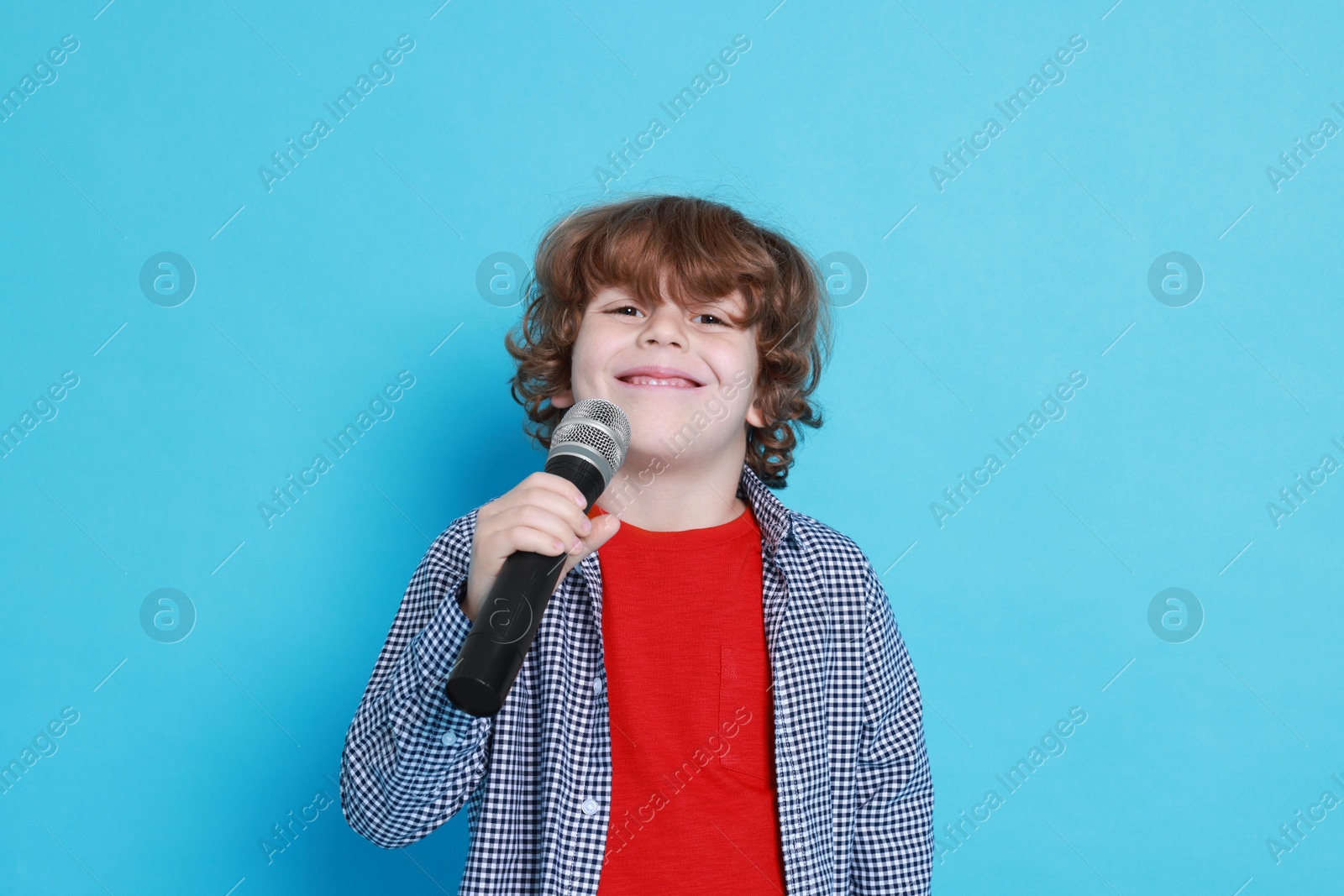 Photo of Little boy with microphone pretending to be singer on light blue background. Dreaming about future profession