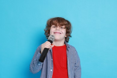 Photo of Little boy with microphone pretending to be singer on light blue background. Dreaming about future profession