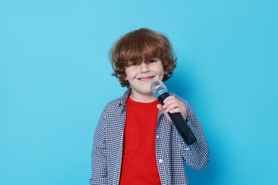 Photo of Little boy with microphone pretending to be singer on light blue background. Dreaming about future profession