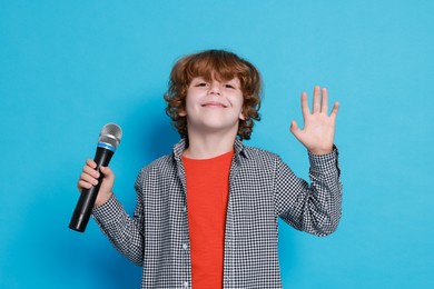 Photo of Little boy with microphone pretending to be singer on light blue background. Dreaming about future profession