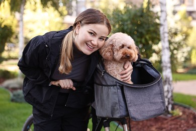 Photo of Woman with bicycle and cute Toy Poodle dog in pet carrier outdoors