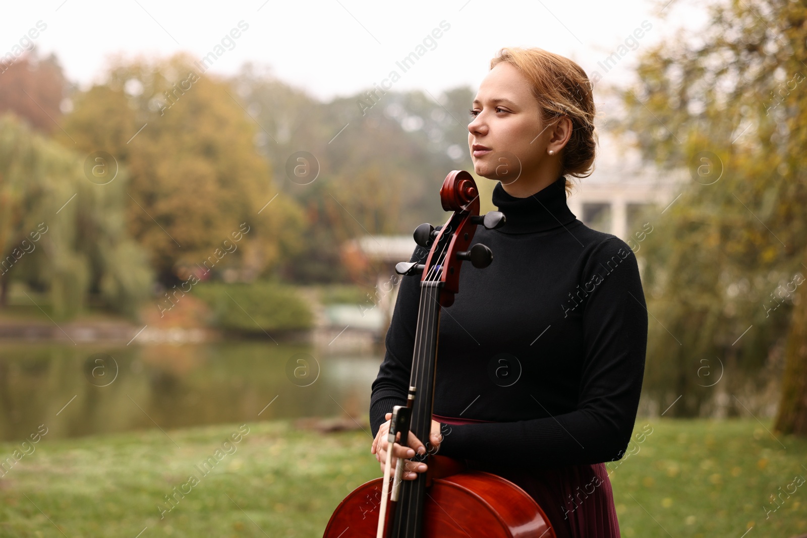 Photo of Beautiful young woman with cello in park, space for text