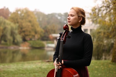 Photo of Beautiful young woman with cello in park, space for text