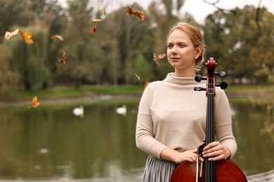 Photo of Beautiful young woman with cello in park, space for text