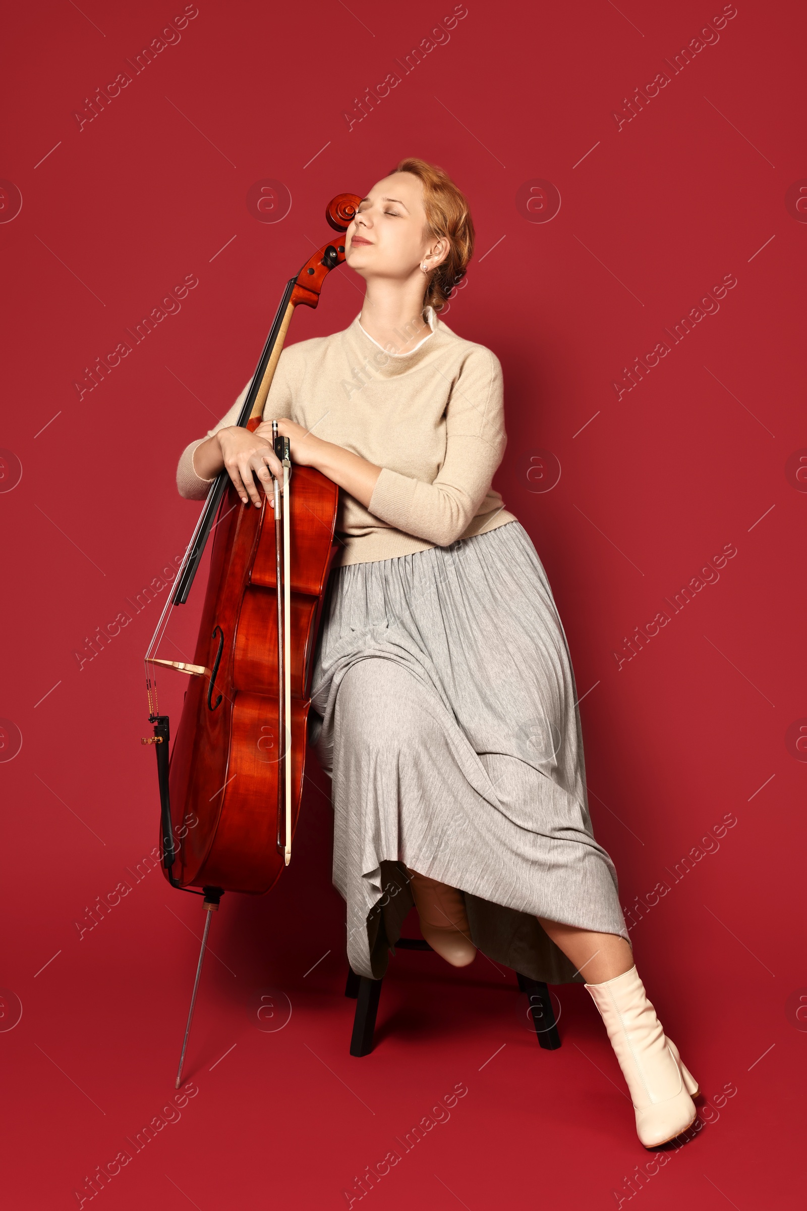 Photo of Beautiful young woman with cello on red background