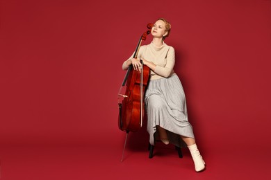 Photo of Beautiful young woman with cello on red background