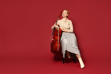 Photo of Beautiful young woman with cello on red background