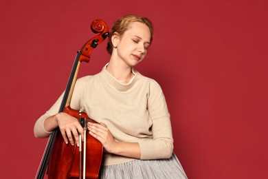 Photo of Beautiful young woman with cello on red background, space for text