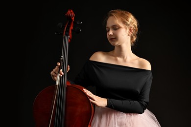 Photo of Beautiful young woman with cello on black background