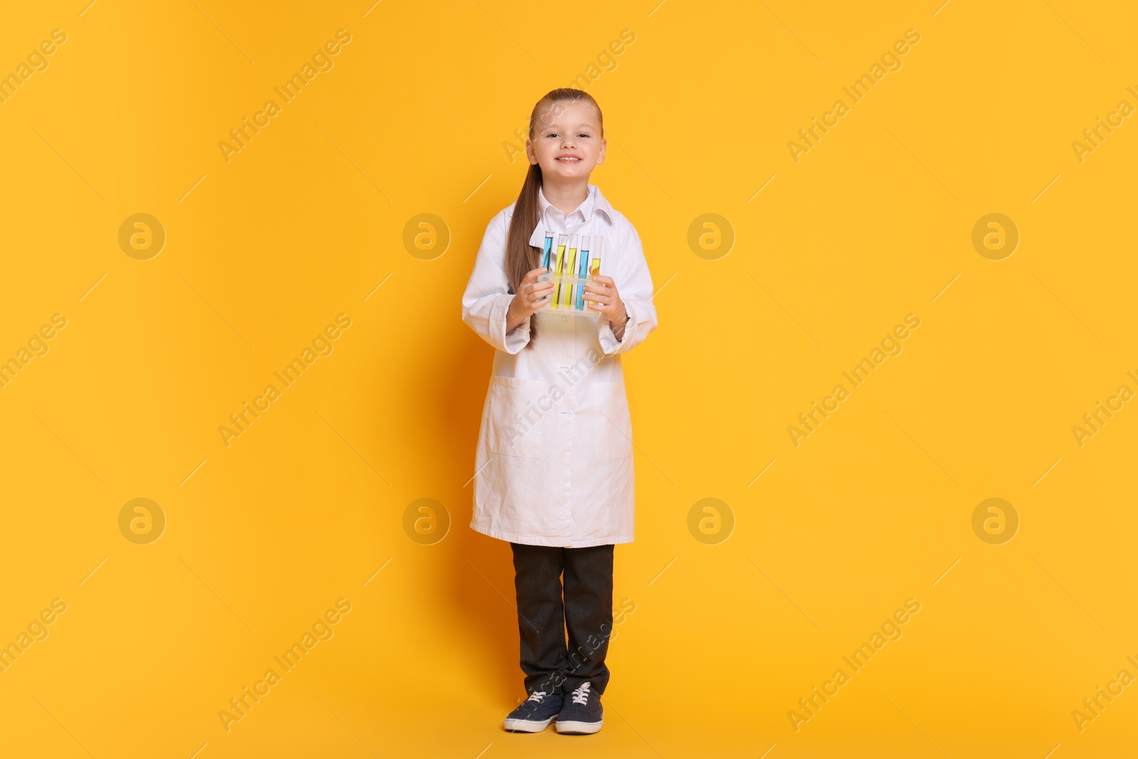 Photo of Little girl with test tubes pretending to be scientist on orange background. Dreaming of future profession