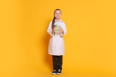 Photo of Little girl with test tubes pretending to be scientist on orange background. Dreaming of future profession