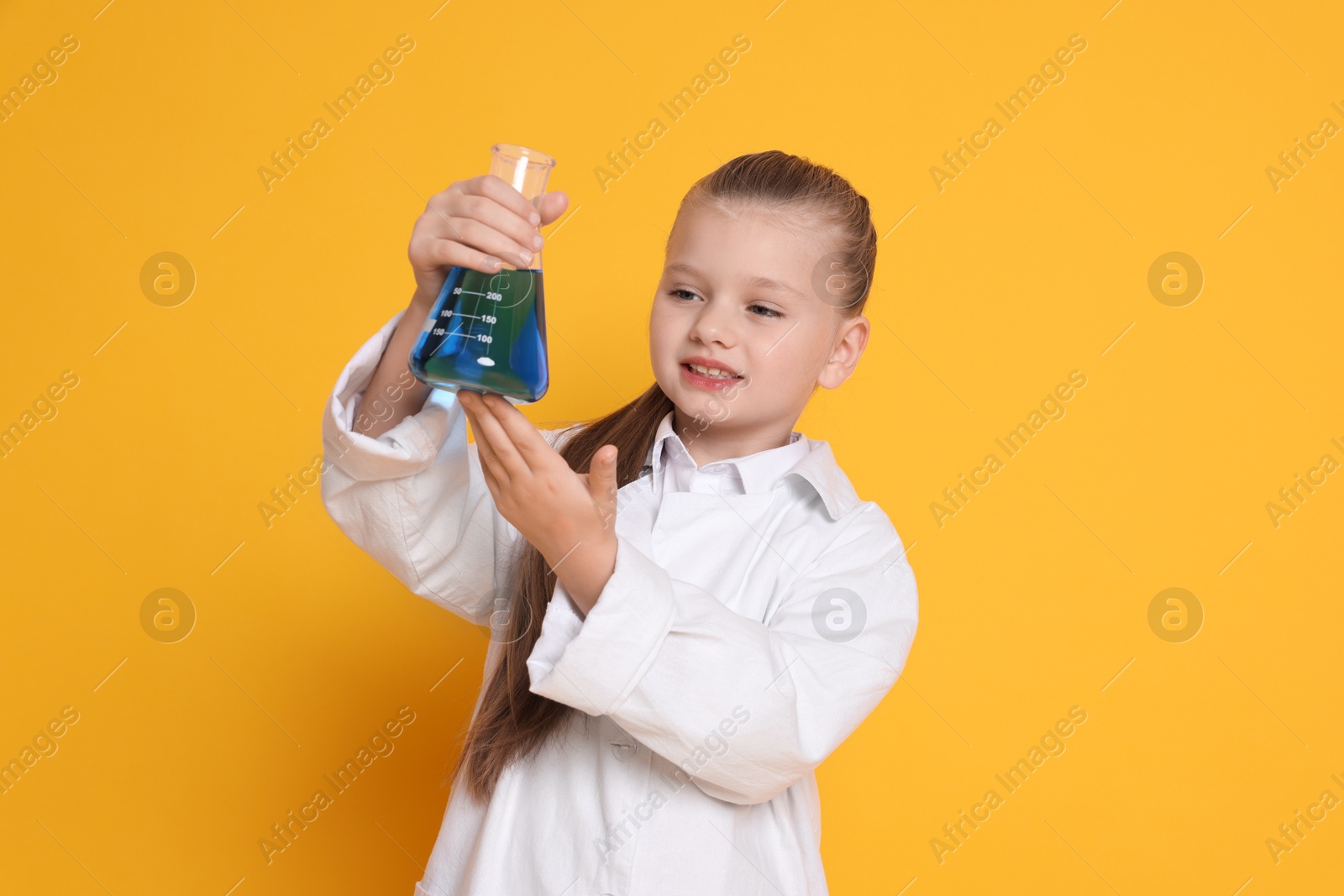 Photo of Little girl with flask pretending to be scientist on orange background. Dreaming of future profession