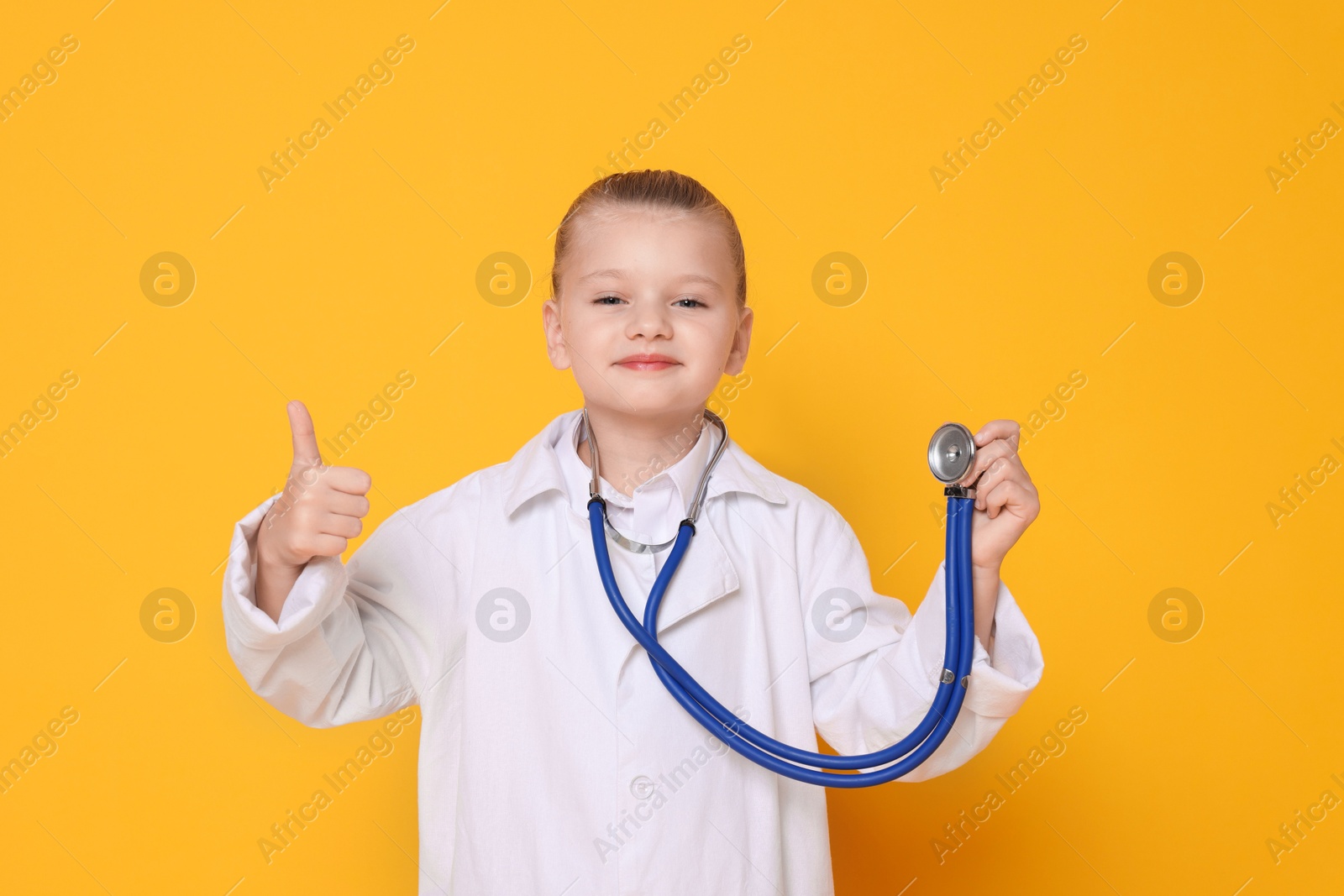 Photo of Little girl with stethoscope pretending to be doctor on orange background. Dreaming of future profession